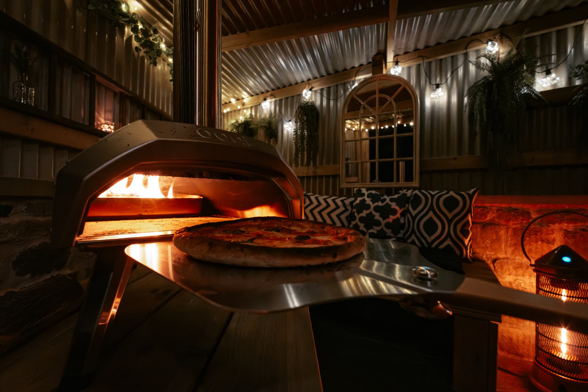 A fresh pizza sliding out of the glowing Ooni oven in the Bothy's pizza shelter