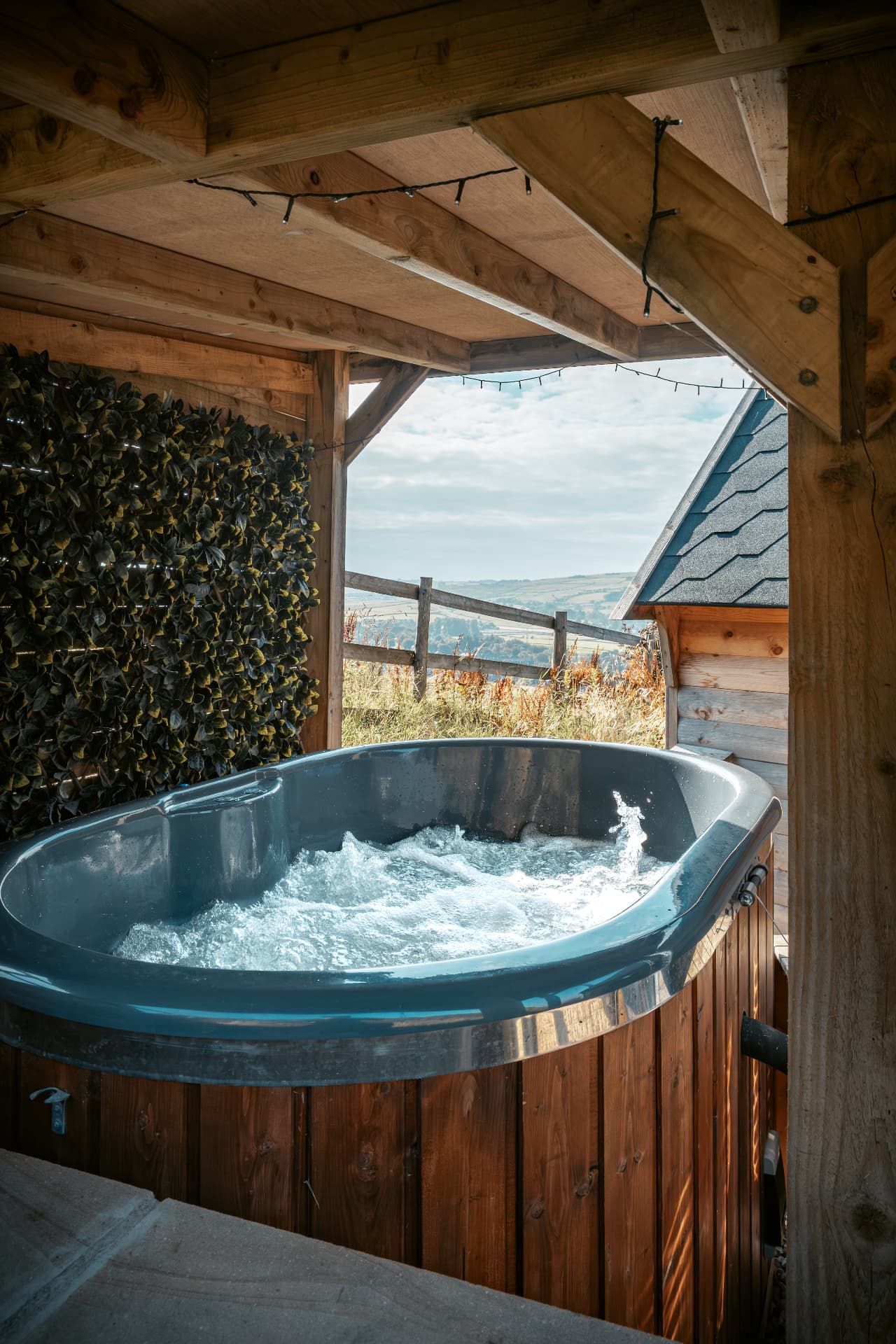Wood-fired hot tub bubbling under the covered deck of The Mallard, looking out over the Yorkshire valley