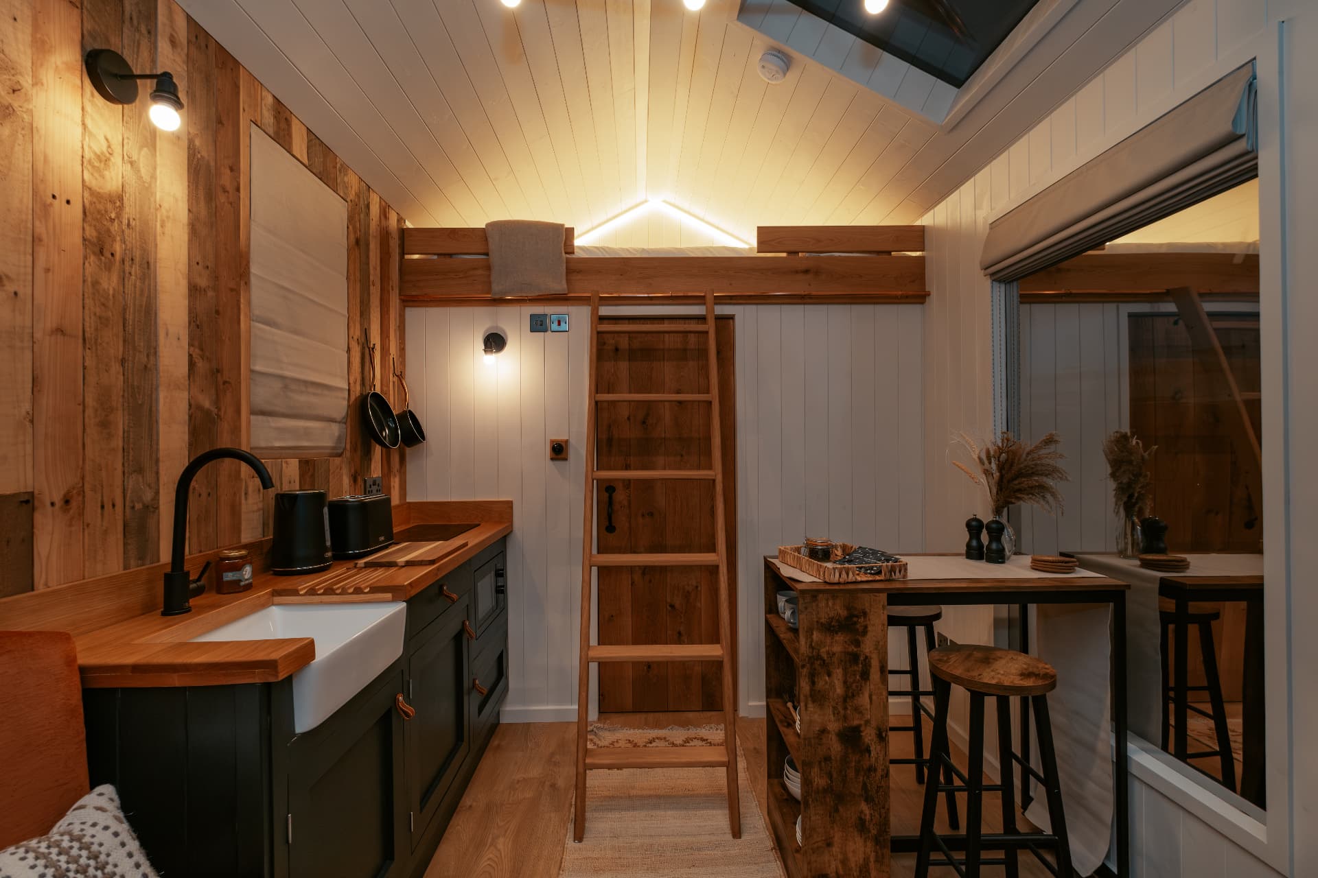 The Bothy kitchen by lamplight at night, with the mezzanine bed above on its oak ladder
