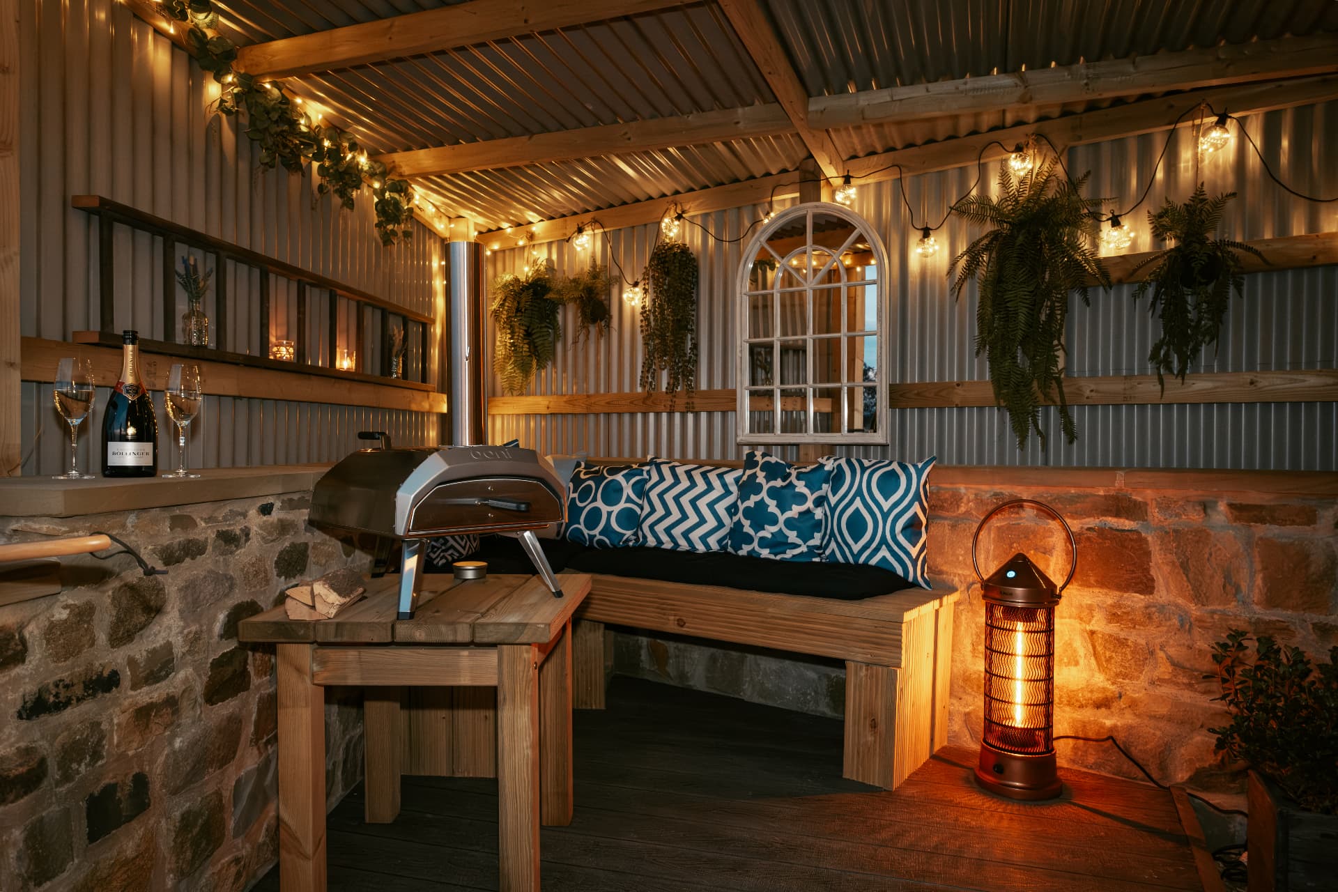 The covered pizza-oven shelter at night — festoon lights, velvet seating and champagne on the bar
