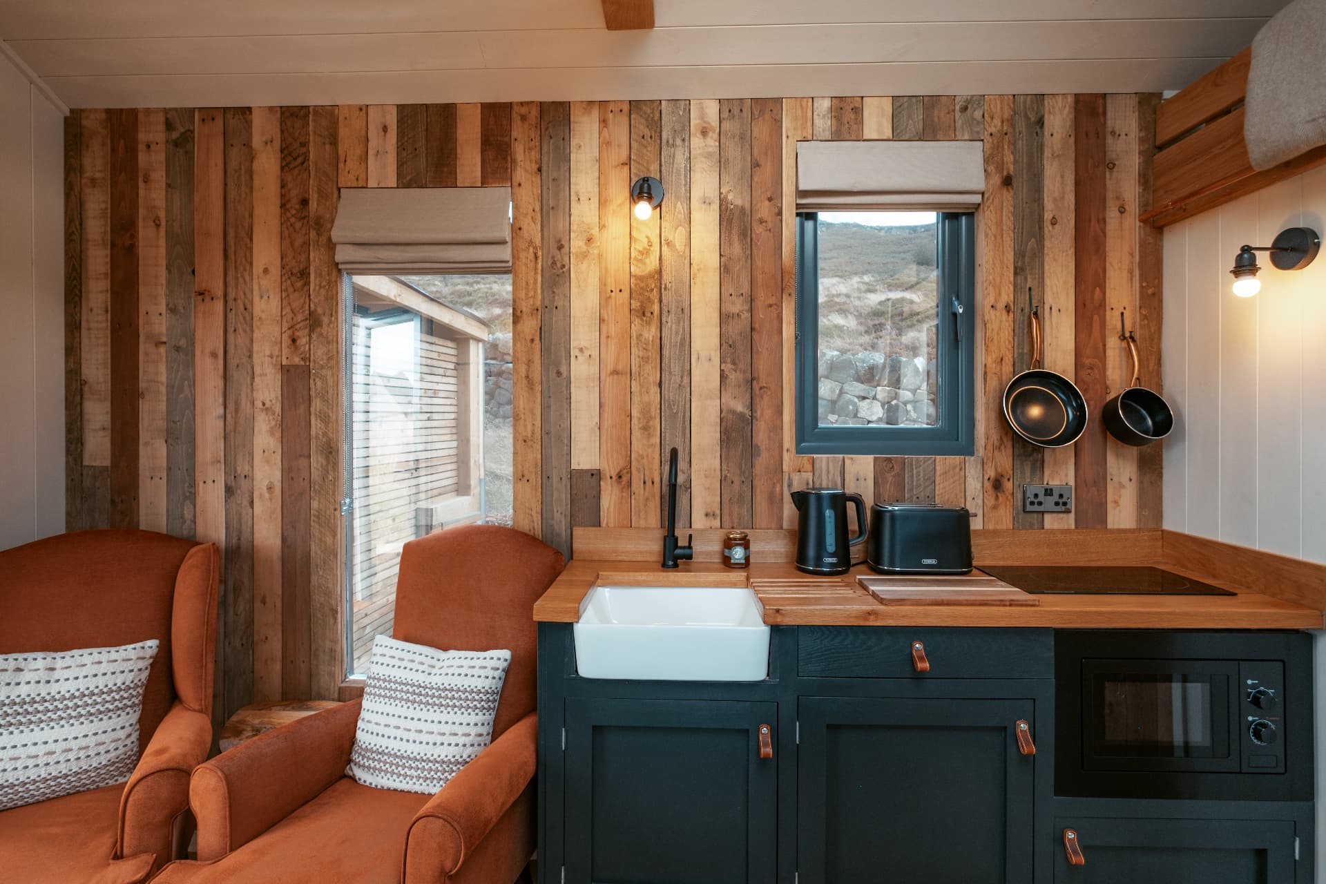 Two velvet armchairs against the reclaimed timber wall in The Bothy, beside the kitchen with its butler sink